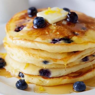Fresh blueberries and bright lemon zest speckle fluffy pancakes, ready to be served hot with butter.