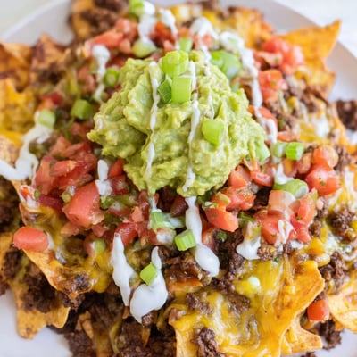 Freshly made guacamole and bright red salsa sit atop hot, cheesy ground beef Beef Nachos, ready to be served at a lively party or game day.