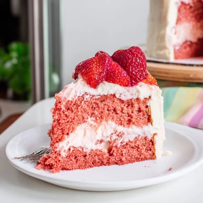 A slice of Strawberry Velvet Cake shows a tender pink crumb and fresh strawberry garnish.