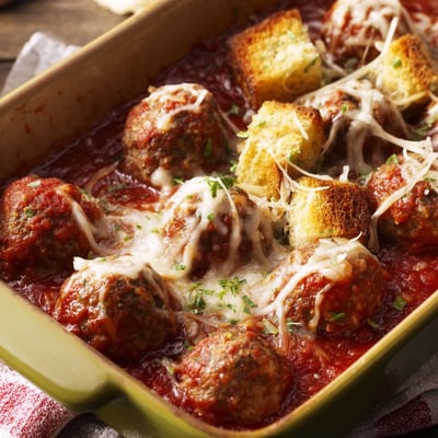 A close-up of the Turkey Meatball and Garlic Bread Bake shows bubbling cheese and herb-flecked sauce, ready to serve from a 9x13-inch baking dish.